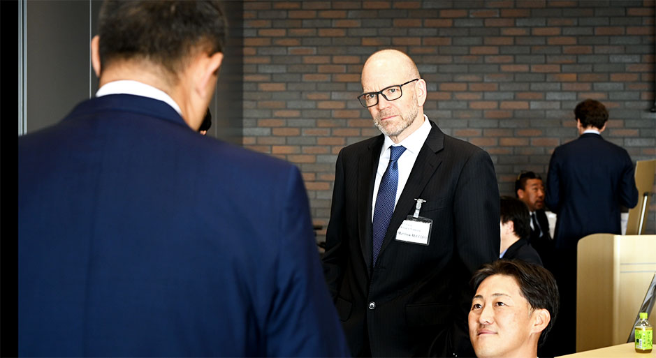 Man wearing glasses and a suit standing in what appears to be a conference or business setting