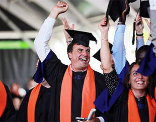Un groupe de diplômés, vêtus de robes de graduation et tenant fièrement leurs chapeaux en l'air. 
