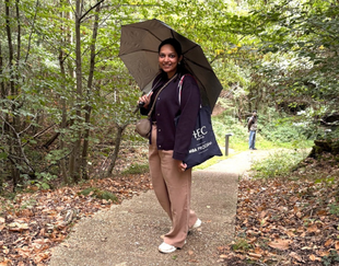 Aayushee Shukla holding an umbrella in the woods of HEC Paris campus