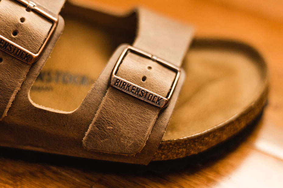 Lanière de sandale Birkenstock en cuir marron avec semelle en liège, isolée sur un fond en bois en gros plan.