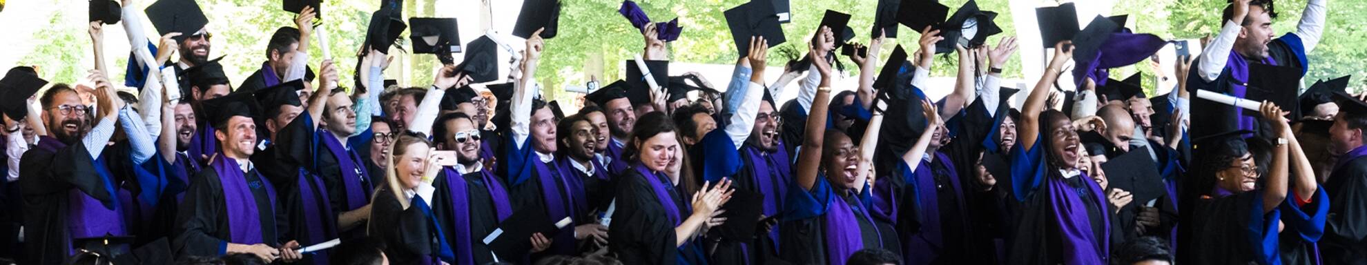 Groupe d'étudiants en robe de graduation célébrant leur cérémonie de remise des diplômes en levant leurs toques noires en l'air, souriants et enthousiastes