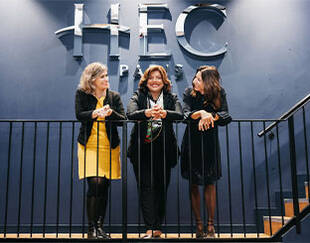 Three smiling women standing in front of a large HBC logo